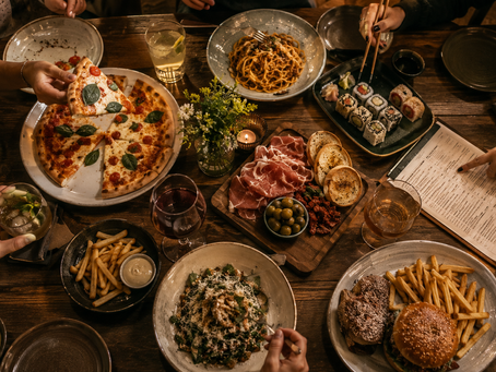 Uma grande mesa de restaurante vista de cima, repleta de pratos compartilhados. Sem mostrar rostos, diferentes mãos revelam os personagens da cena: uma dividindo cuidadosamente a pizza, outra alcançando discretamente o prato do vizinho para experimentar, alguém apontando indeciso para o cardápio, enquanto outra segura tranquilamente o mesmo pedido de sempre. A composição deve transmitir humor, reconhecimento e humanidade.