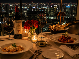 Mesa elegante para dois em restaurante sofisticado de São Paulo, com massas artesanais, vinho tinto, velas acesas e a cidade iluminada ao fundo. Atmosfera intimista, cinematográfica e romântica, transmitindo a ideia de que a gastronomia pode transformar uma noite comum em uma memória inesquecível.