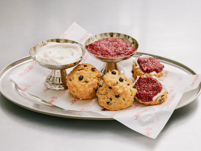 Scones vegan avec crème coco et confiture de framboises sur papier alimentaire Jacquie Club, brandé avec le logo conçu par Secousse Studio.