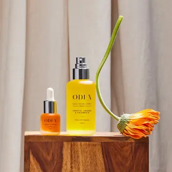 Huile sèche et sérum visage Oden, accompagnés d’une fleur courbée – photographie produit stylisée.