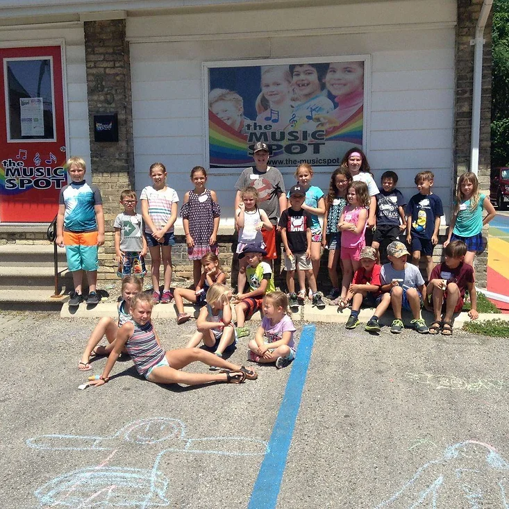 a group of students sit outside of the music spot for a group photo, showing off some chalk art