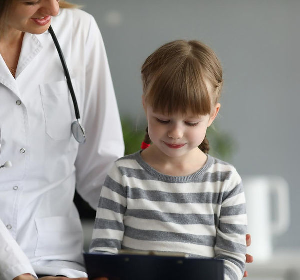 Doctor in white coat with stethoscope talks to a young girl wearing a striped shirt. They are smiling in a bright, profession