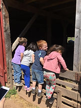 Four children standing on a fence to peer into the opening of a red barn