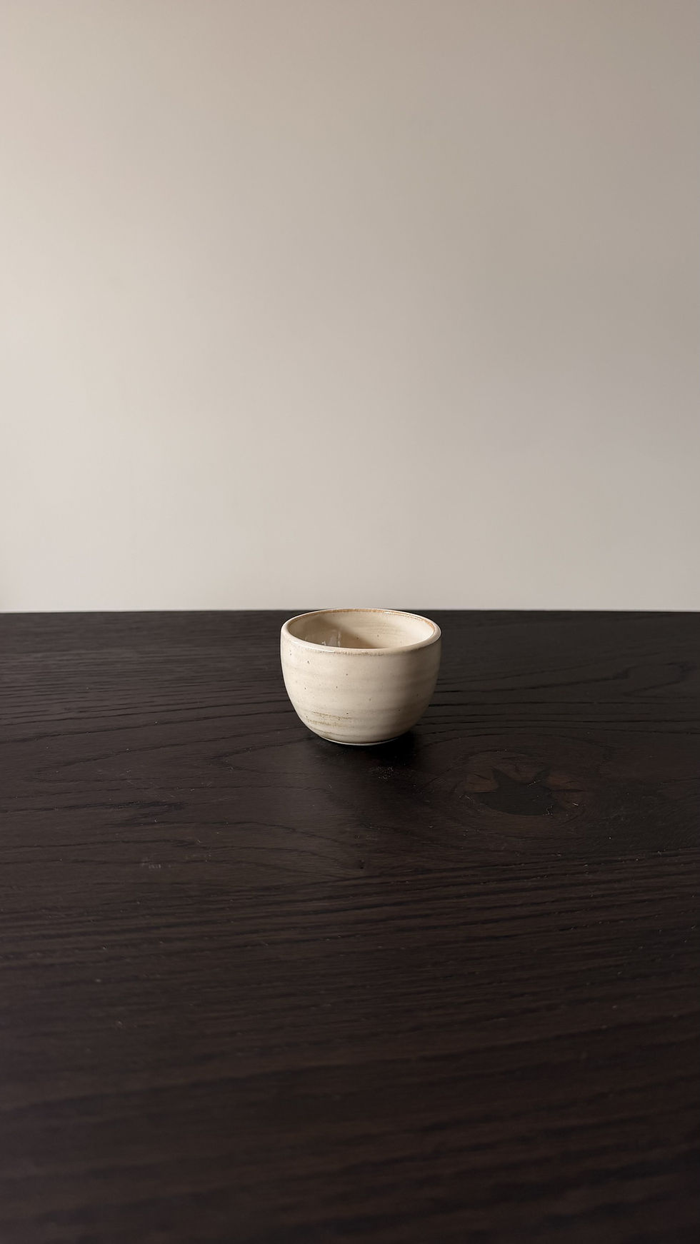 Handgemaakt beige keramieken kopje met glanzend glazuur op donkere houten tafel