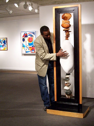 Charles Wright in jacket and geans explaing large stone sculpture in an Art Gallery.