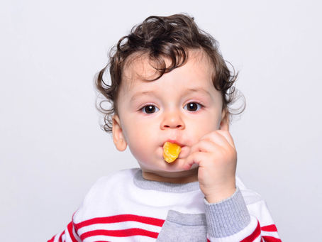Bebé comiendo un gajo de mandarina con la mano, ilustrando el proceso de alimentación complementaria y el desarrollo de habilidades de alimentación en la primera infancia.