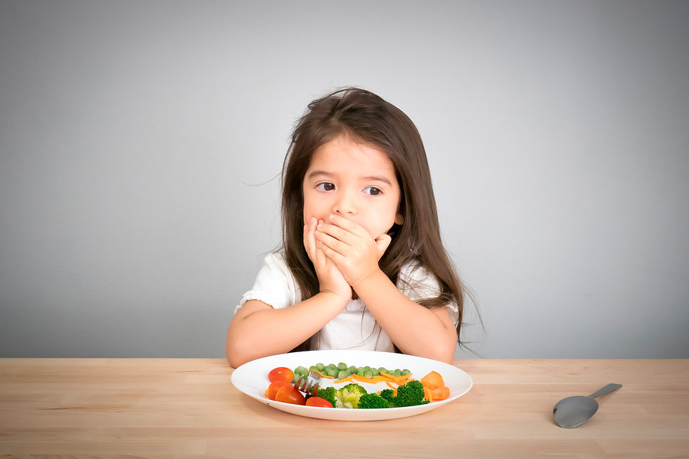 Niña cubriendo su boca con las manos frente a un plato de verduras, representando la selectividad alimentaria en niños y el rechazo a los alimentos en la primera infancia.