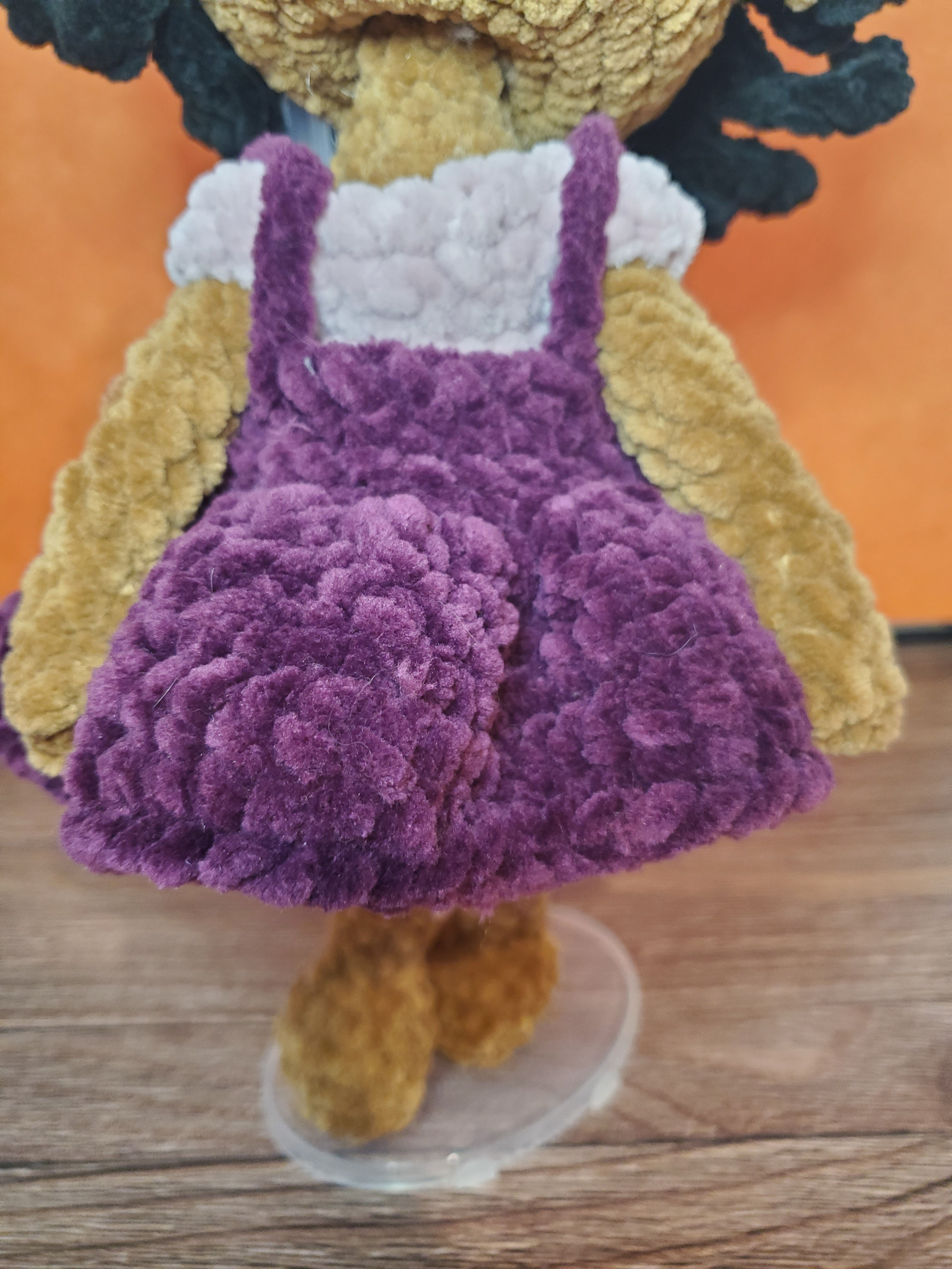 crochet doll pinafore in a dark purple over a light purple dress.