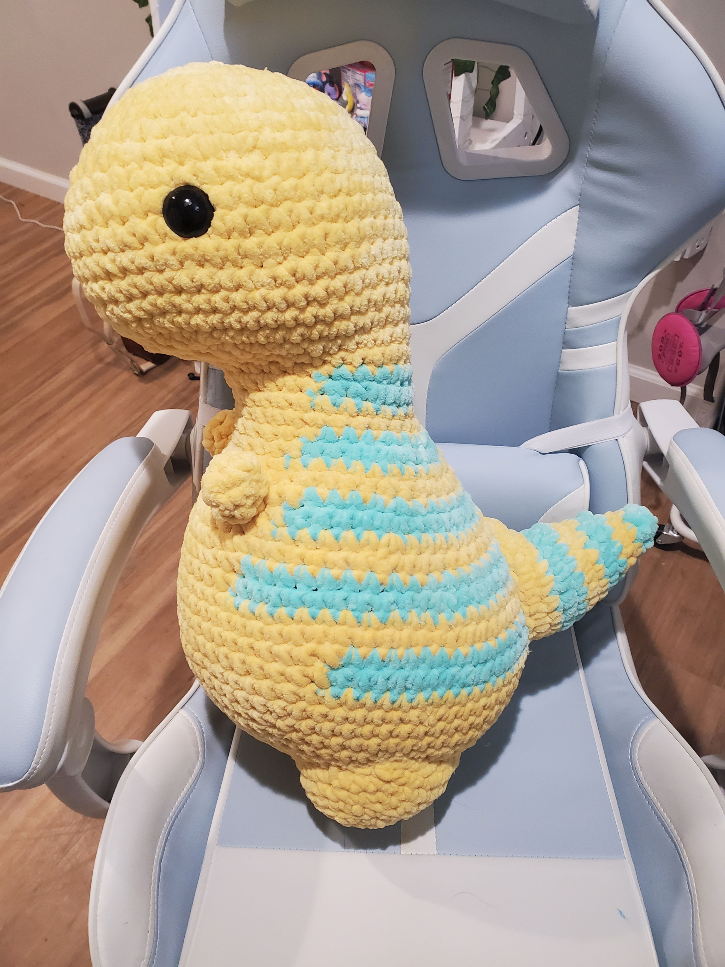 Jumbo t-rex with a yellow body and teal stripes sitting in a blue desk chair.