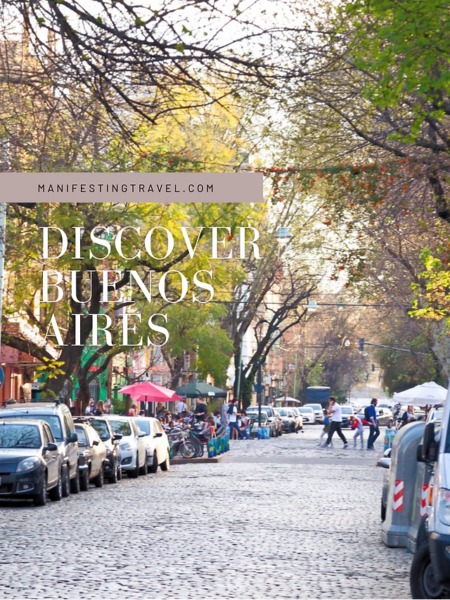 A leafy green street lined with cars, artisan stalls, and pedestrians walking about