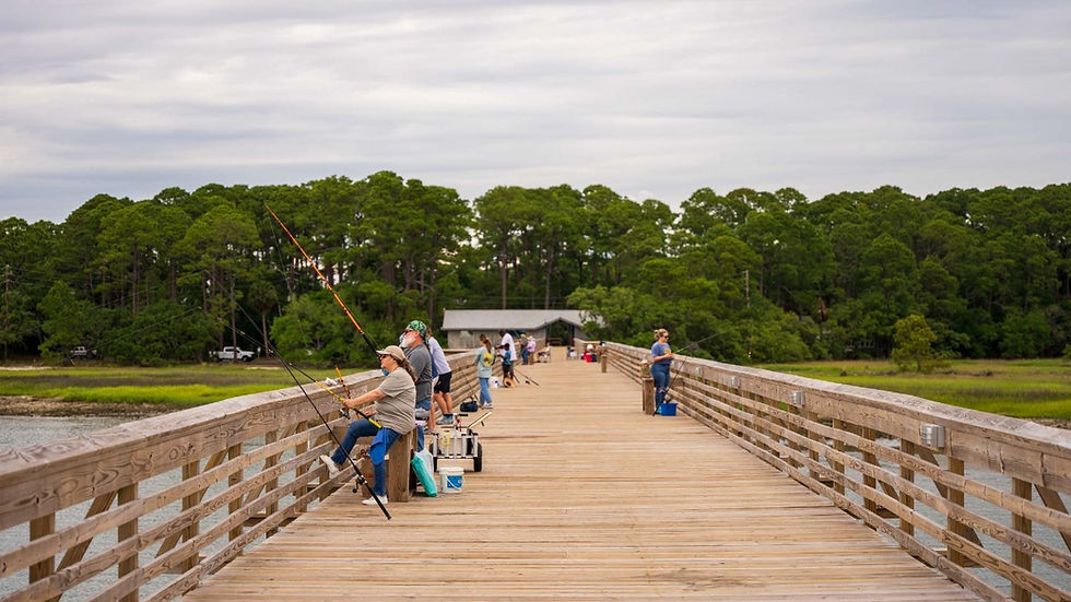 The Hunting Island Pier with people fishing from the dock, and a green maritime forest in the background. ©AlonzoWright for Manifesting Travel.