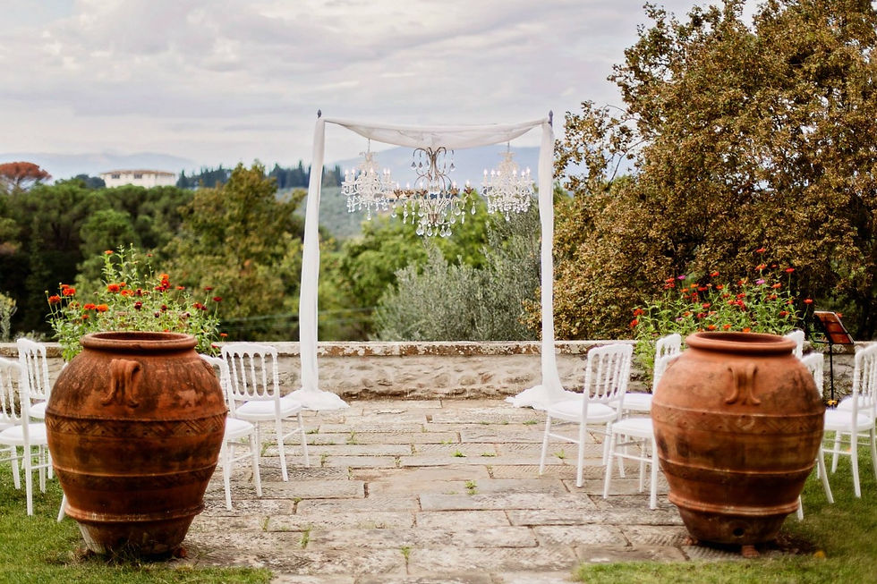 A wedding ceremony overlooking the Tuscan vineyards with three hanging chandeliers, terra cotta urns and Italian villas in the background of this wedding in Italy. Featured in Managing a destination wedding budget on fluctuating currency for Manifesting Travel