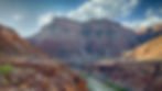 The inside of the Grand Canyon with jutting rigid desert mountains, helicopters and the Colorado River below.