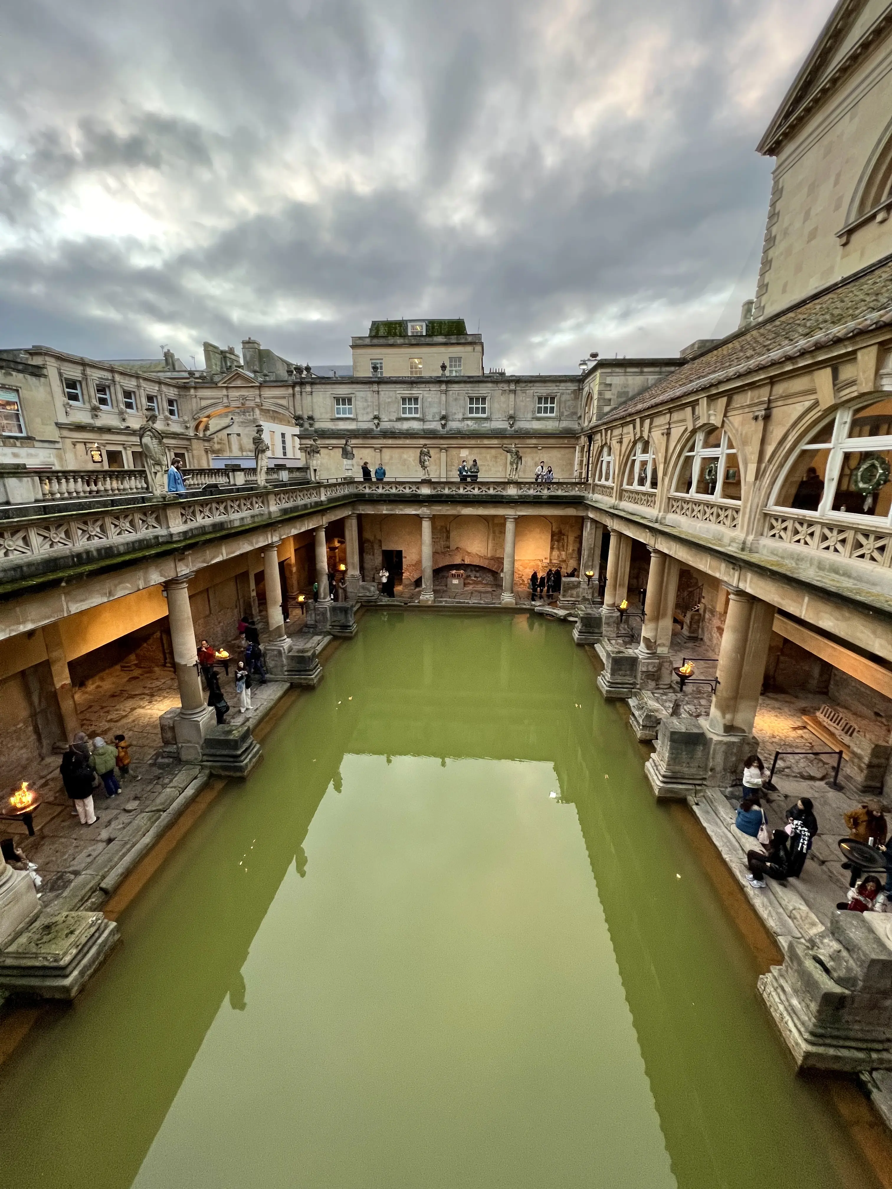 A view of the Roman Baths in Bath, England from the second floor gallery under a cloudy sky ©AOnozWright