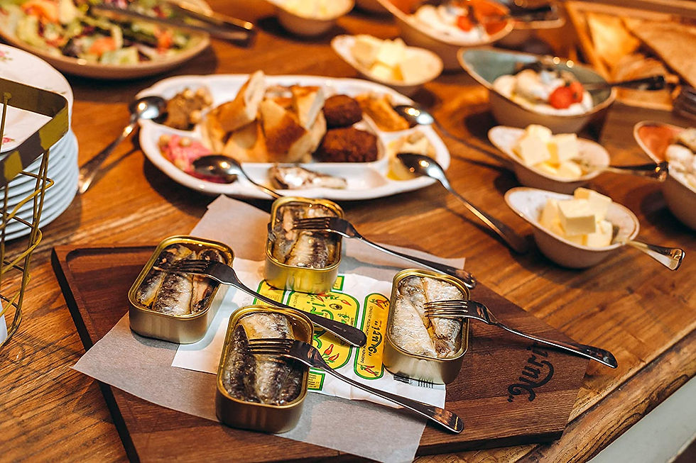 A wooden table full of different foods including canned sardines. One of the more unique travel gift ideas comes from Portugal, a huge foodie travel destination. Photo courtesy of NURI Portuguese Sardines for travel gift ideas featured in Manifesting Travel