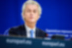 Geert Wilders speaking at a podium with "europarl.eu" visible. Blue background with text. Serious expression, wearing a suit and blue tie.