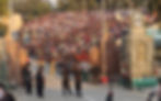 Border ceremony with uniformed guards performing, large crowd in stands cheering. Stone columns display inscriptions. Energetic atmosphere.