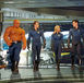 Four people (Fantastic Four: Rise of the Silver Surfer) in futuristic suits walk confidently in a high-tech, metallic room. One has an orange, rocky texture. Mood is determined.