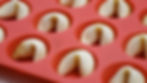 Fortune cookies in a red silicone baking mold, neatly arranged. The cookies are light brown with a smooth texture.