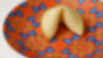Fortune cookie on a vibrant orange plate with blue butterfly patterns. The setting is bright, highlighting the cookie's golden color.
