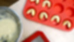 Red tray with fortune cookies, next to a mixing bowl of batter on a light wood table. Red silicone mat partially visible.