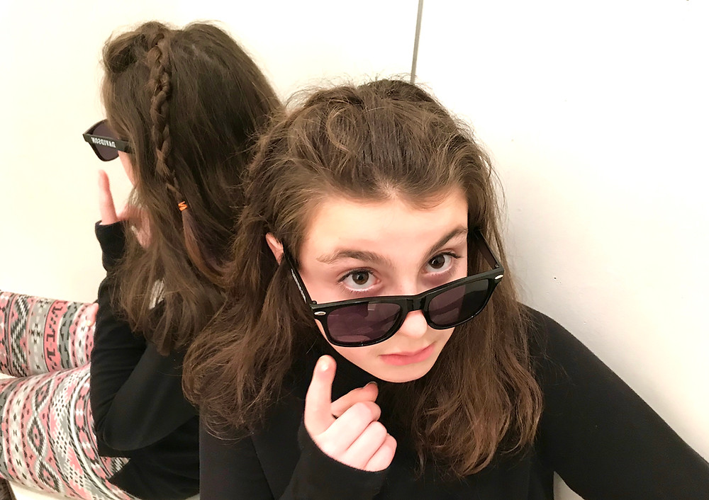Image of a teen girl sitting against a mirror, looking over the top of her sunglasses. Raleigh psychotherapy, counseling, Katherine Broadway