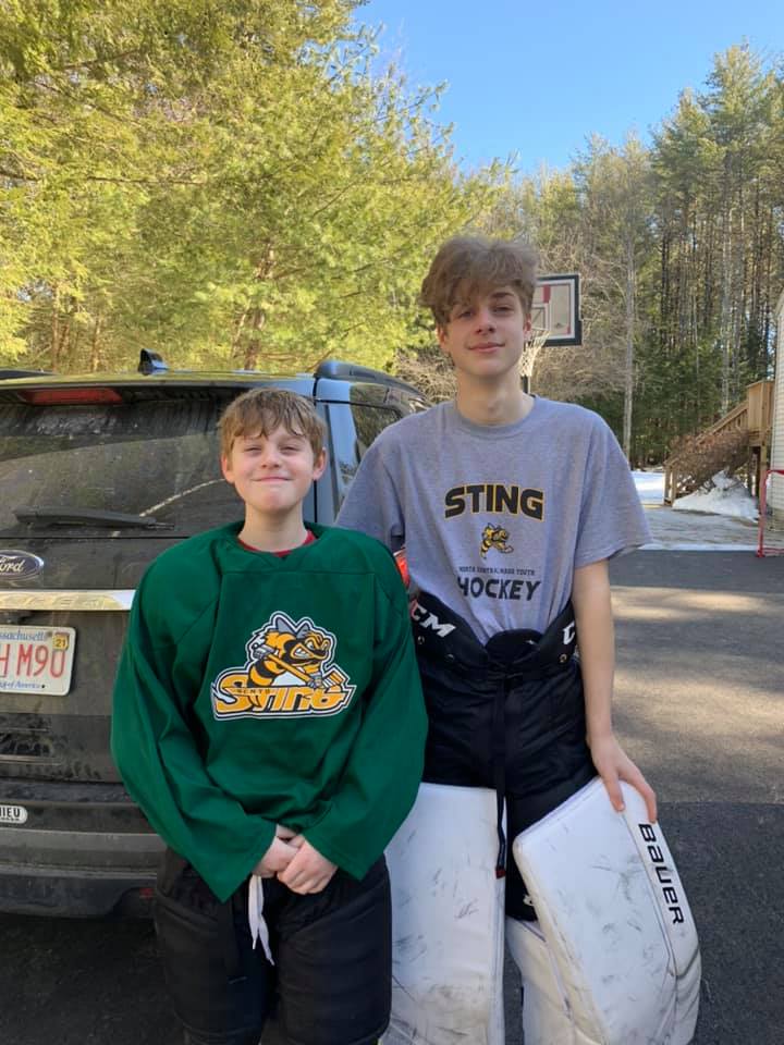 two brothers, carter and cohn, in hockey gear, standing next to eachother outside and posing for a photo