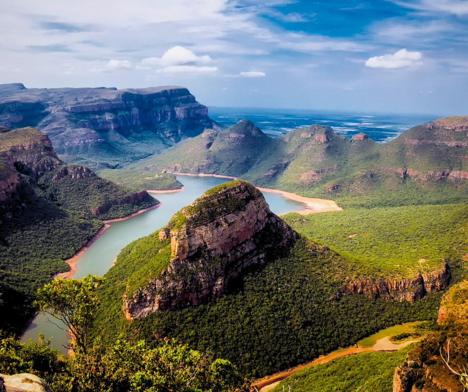 Scenic view of a winding river through lush green mountains under a partly cloudy blue sky. Vibrant landscape with a tranquil mood.