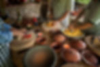 People in checkered aprons chop and mix colorful ingredients in a rustic kitchen with candles, clay pots, and a relaxed, warm atmosphere.