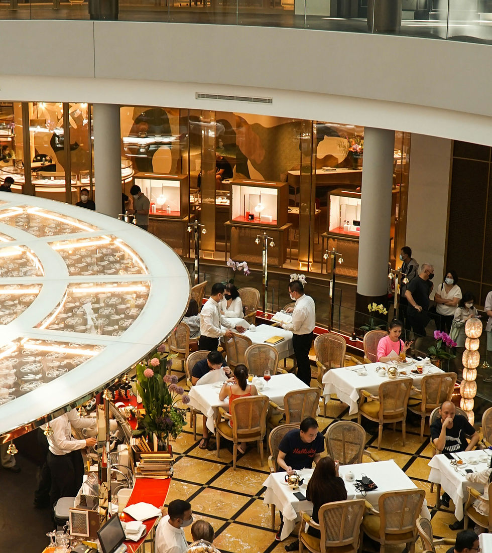 Elegant mall restaurant with masked diners and waiters at white-tablecloth tables, warm gold decor and glass storefronts.