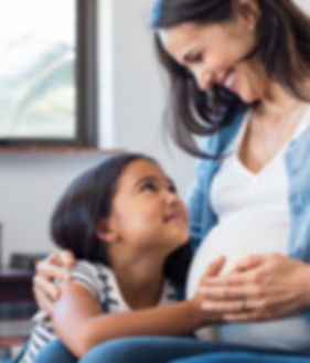 Pregnant mom and daughter smiling and hugging