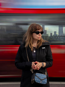 Woman in sunglasses standing in front of a moving red London bus