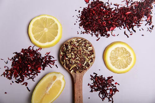 A product shot of Erva Brew’s Hibiscus-Lemon Yerba Mate in a wooden spoon, decorated with lemon wedges kept around and loose hibiscus leaves.