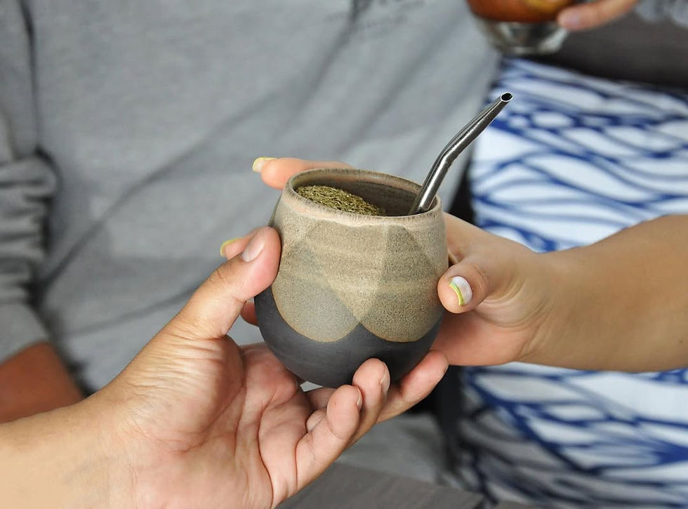 Two people sharing a ceramic guampa filled with yerba mate, with a bombilla inside.