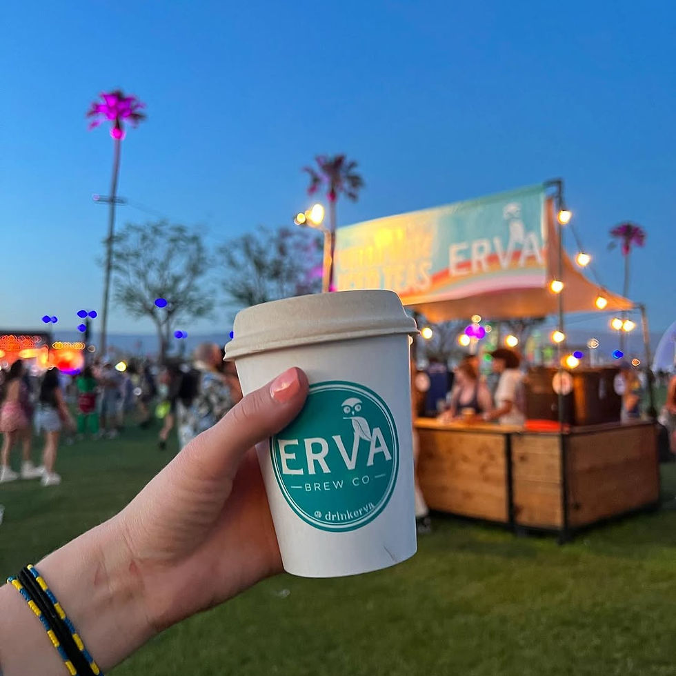 A person holding up an Erva Brew cup in front of an Erva Brew stall with a lively crowd in the background.