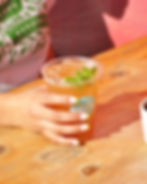 A person holding an Erva Brew iced yerba tea garnished with mint leaves, resting on a table.