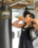Boxer training with gloves on, drinking Erva yerba mate blend beside a boxing bag.