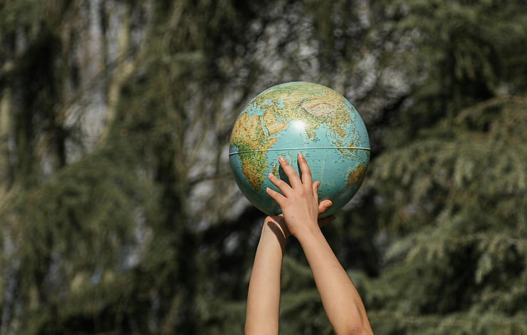 Manos levantando una bola del mundo en un bosque