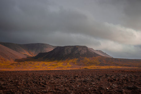 A hill near Kleifarvatn lake, Iceland. The sky is moody and somewhere to the right, out of shot, the sun casts long shadows across the ridgeline.