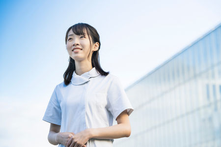青空の下で微笑む白衣姿の看護師の女性