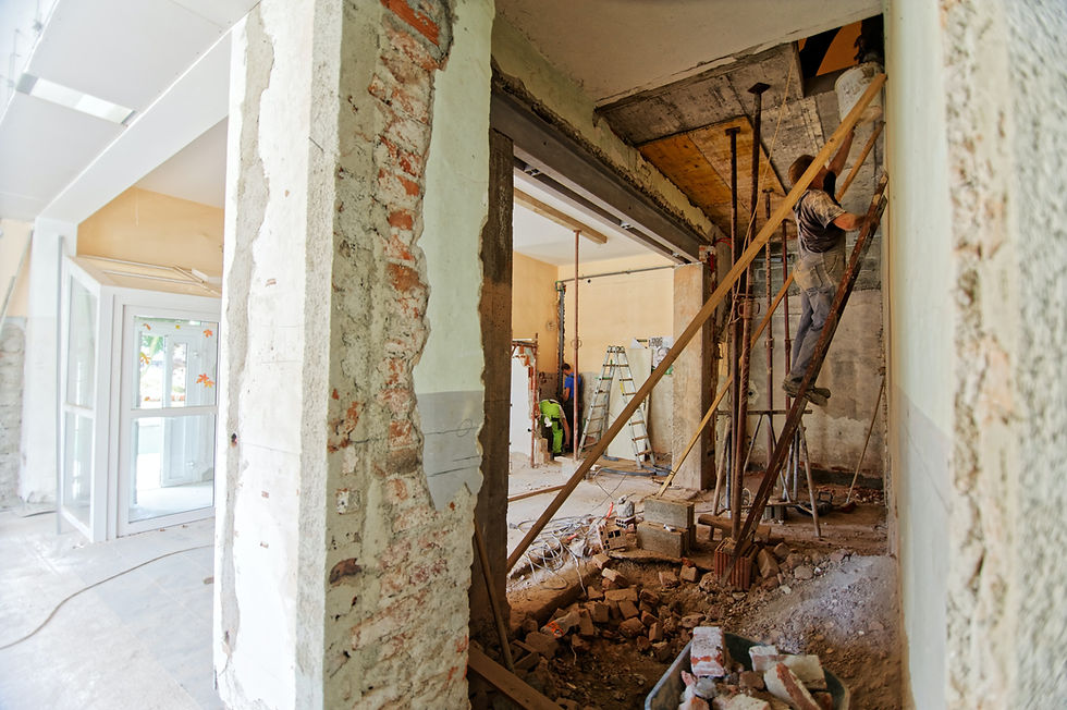 "Interior construction site with exposed brick walls and workers performing renovation tasks, using scaffolding and ladders in a partially demolished building space."