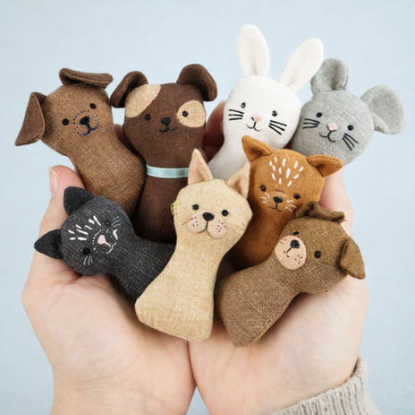 Handen die meerdere kleine handgemaakte stoffen dieren vasthouden, waaronder konijnen, katten en hondjes in natuurlijke kleuren.