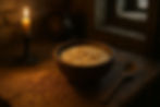 A rustic wooden bowl of creamy frumenty porridge sits beside scattered wheat grains and a wooden spoon on a rough-hewn kitchen table, illuminated by warm candlelight through a stone window.