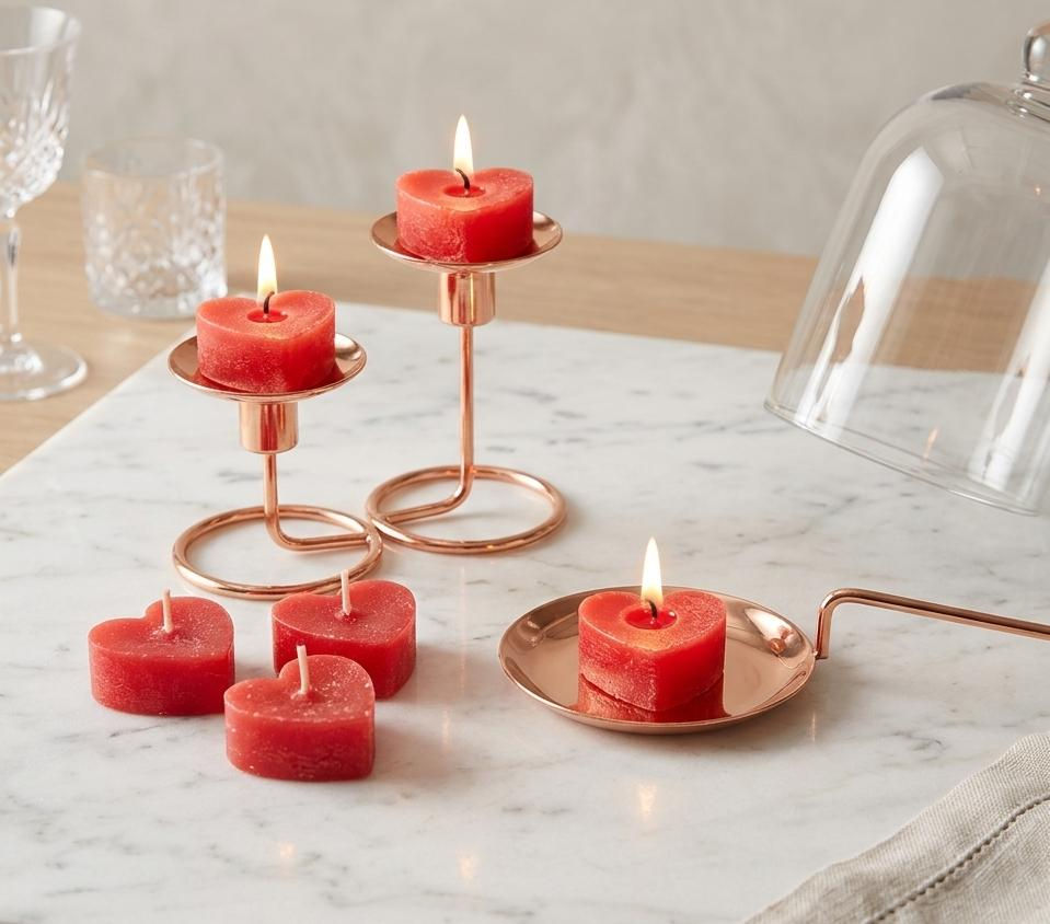 Velas vermelhas de coração em castiçais de cobre, algumas acesas.
