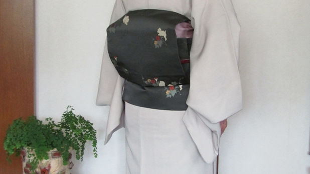 黒地に花柄の帯を付けた薄紫色の訪問着女性の後ろ姿