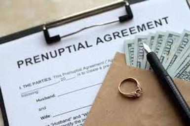 Prenuptial agreement covered by wedding rings and envelope of money, symbolizing the costs of marriage.