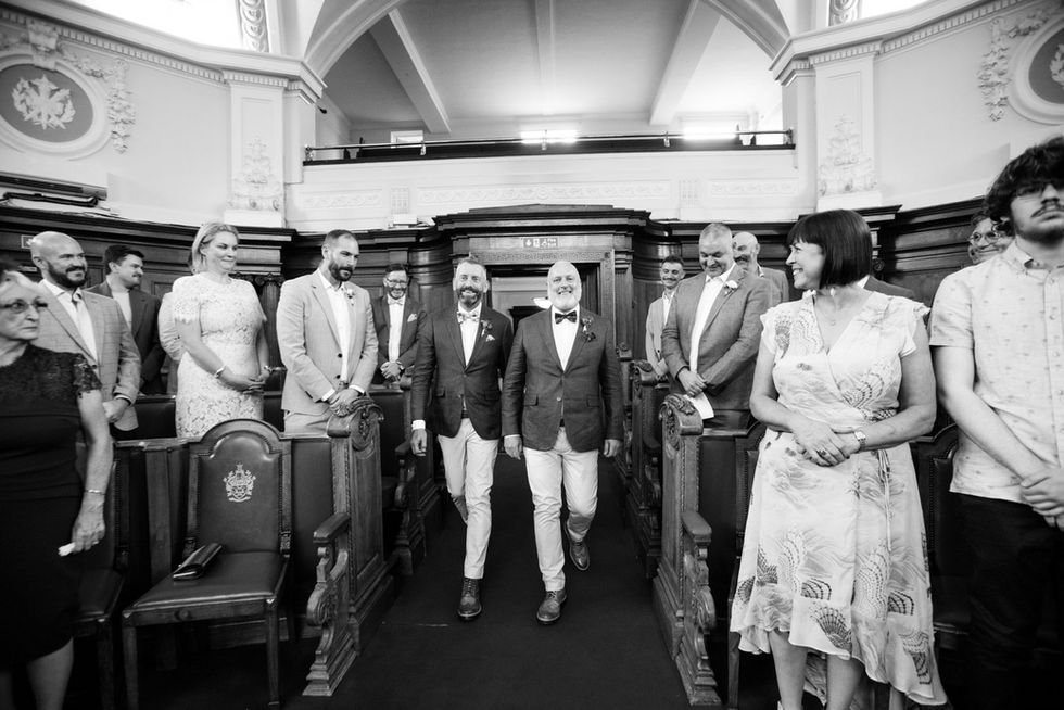 Two grooms walking down the aisle, wedding guests watching