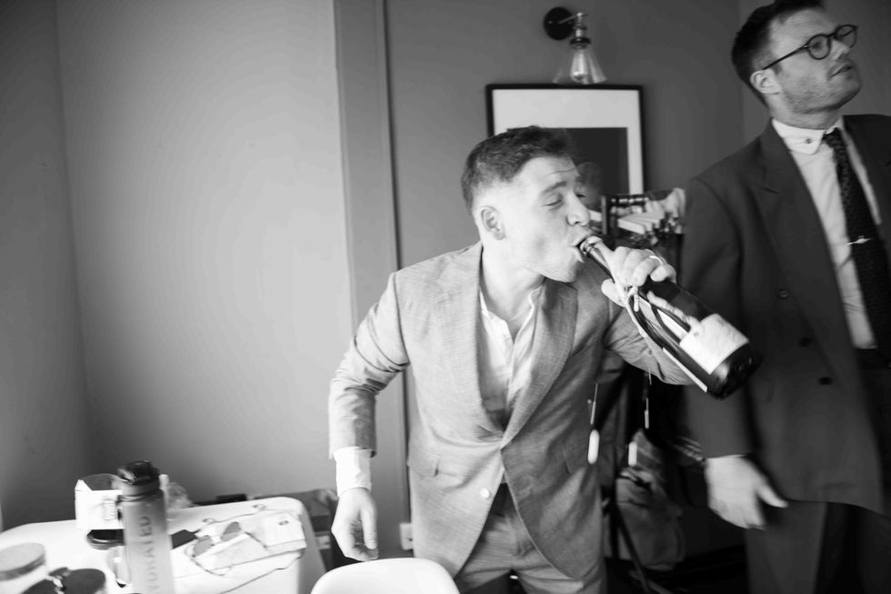 Man in suit drinks champagne bottle; wedding photo