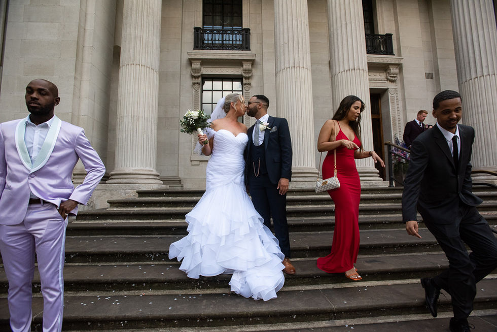 Bride and groom kissing on steps, wedding party in background