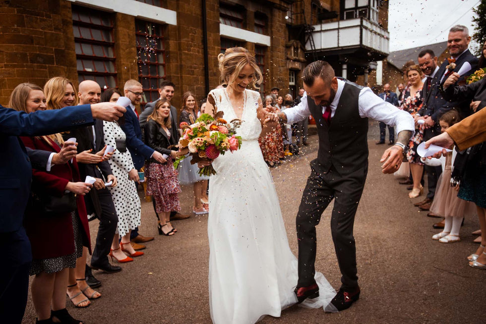 Groom tripping on wedding dress as they walk through confetti at Hook Norton Brewery wedding